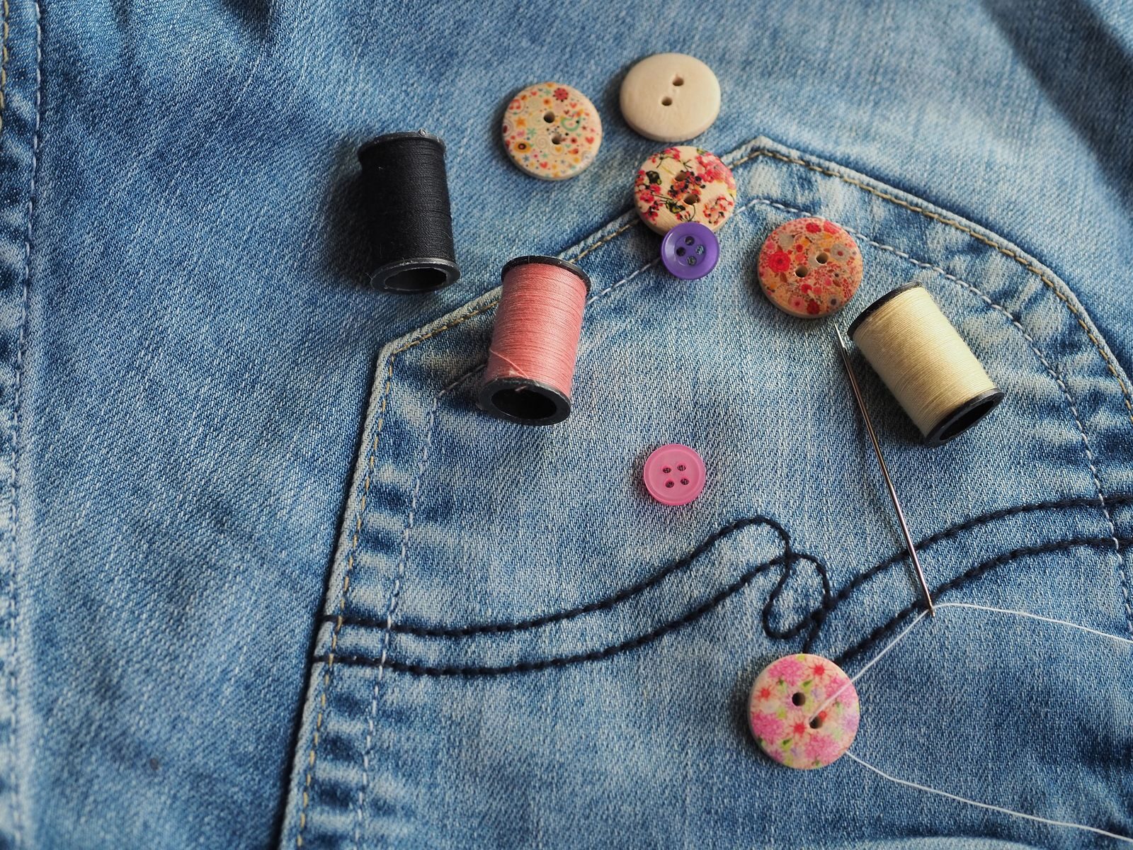 Creative flat lay of sewing materials on blue denim pocket showcasing buttons and thread spools.