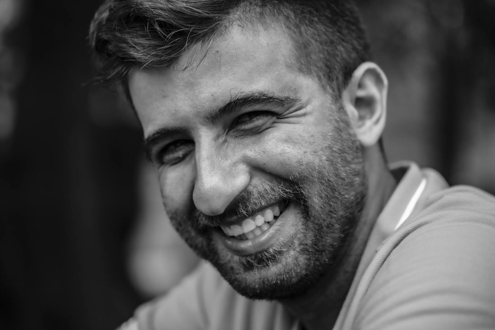 Close-up black and white portrait of a smiling man with a beard.