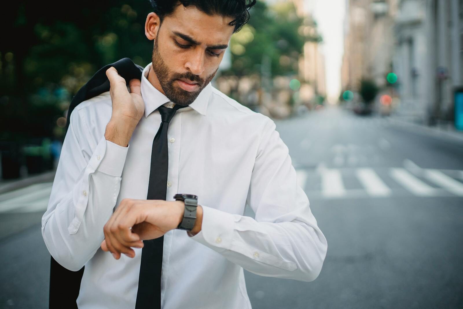 Confident businessman checks his watch in an urban street, symbolizing punctuality.