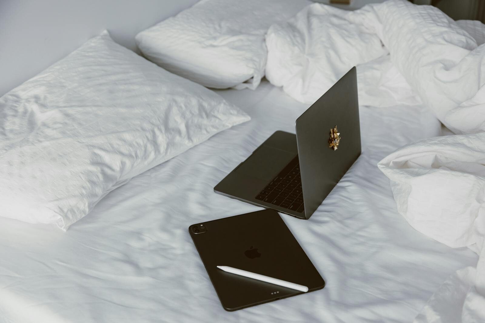 A modern home office setup with a laptop and tablet on a white bed, perfect for remote work or leisure.